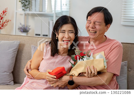 Joyful senior couple laughing together with gifts and flowers on Valentine's Day Joyful senior couple laughing together with gifts and flowers on Valentine's Day 130221086