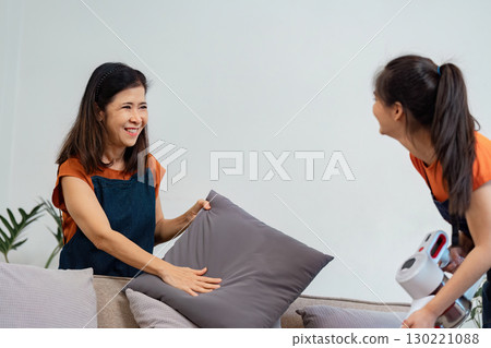 Mother and daughter arranging pillows while cleaning the living room 130221088