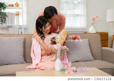 Senior couple celebrating Valentine's Day with a gift and flowers at home 130221128