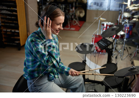 Cute woman is wearing headphones while playing a drum set in a music store Cute woman is wearing headphones while playing a drum set in a music store 130223690