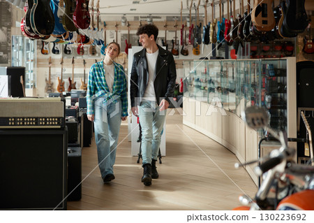 A man and a woman walk through a guitar store, exploring instruments A man and a woman walk through a guitar store, exploring instruments 130223692