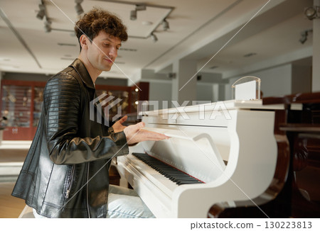 A man in a black leather jacket preparing to play a white piano 130223813