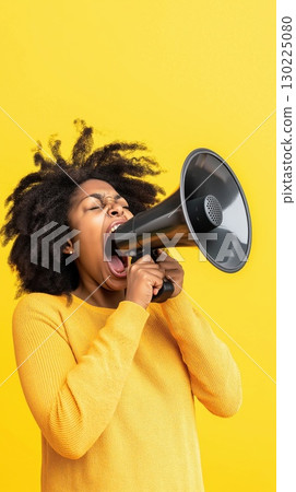 Afro haired woman wearing bright yellow sweater shouting through megaphone with passionate expression against vivid yellow background 130225080