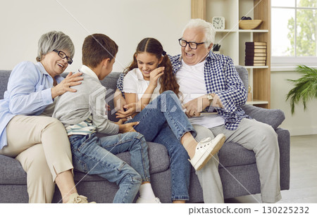 Happy grandparents tickling grandchildren while sitting on the sofa all together 130225232