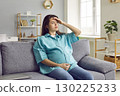 Young pregnant woman sitting on sofa, having a headache, feeling a bit sick and tired 130225233
