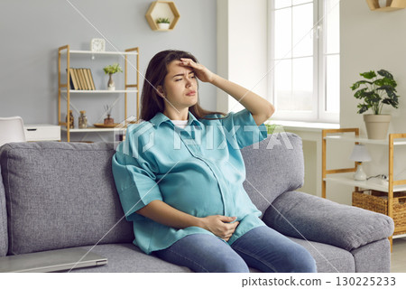 Young pregnant woman sitting on sofa, having a headache, feeling a bit sick and tired 130225233