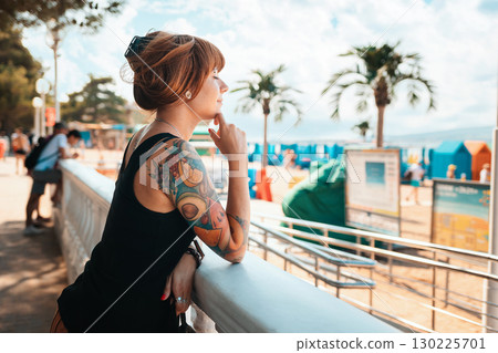Portrait of a young smiling woman with a tattoo on her arm, looking at the sea. There is a beach in the background. The concept of summer vacation 130225701