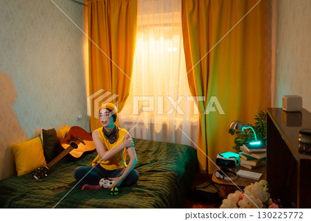Relaxed young girl in a cozy room spends time playing video games after school. Concept of balance between rest and modern technology. Wide shot Relaxed young girl in a cozy room spends time playing video games after school. Concept of balance between rest and modern technology. Wide shot 130225772