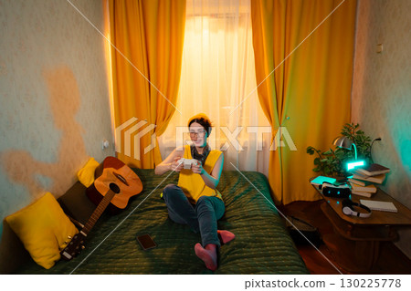 Teen girl in colorful hat and vest looks excited while playing a console game. Concept of emotional expression and fun. Wide shot 130225778