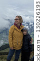 Mother and son standing on a mountain top, overlooking a breathtaking landscape. Both are dressed warmly, sharing a joyful and content moment amidst the natural beauty. 130226193