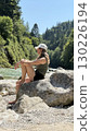 Woman Relaxing on Riverbank Rock Amidst Nature 130226194