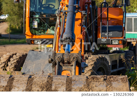 A close view of a powerful excavator, showing its hydraulic arm and bucket, positioned at a construction site with clear sky 130226360