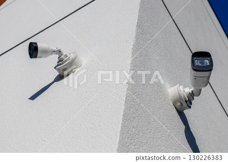 Surveillance cameras are securely installed at the corner of a building, capturing activity under bright daylight Surveillance cameras are securely installed at the corner of a building, capturing activity under bright daylight 130226383