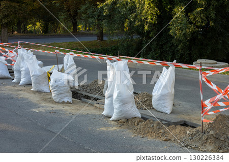 Construction work is taking place along the roadway with sandbags and safety barriers marking the area for public safety Construction work is taking place along the roadway with sandbags and safety barriers marking the area for public safety 130226384