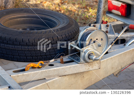 Close-up of a pulley system attached to a trailer with a spare tire, showcasing its practical design and functionality in bright sunlight Close-up of a pulley system attached to a trailer with a spare tire, showcasing its practical design and functionality in bright sunlight 130226396