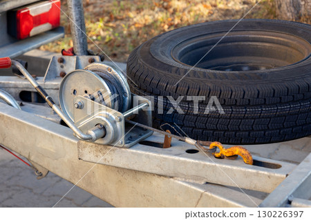 A winch system is set up on a trailer to assist in lifting and storing a spare tire, with sunlight illuminating the setting 130226397