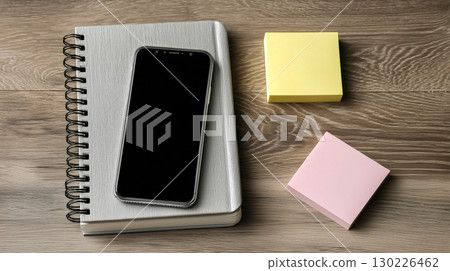 智慧型手機和筆記本放在木桌上,上面貼著黃色和粉紅色的便籤,位於一個辦公室風格的、井然有序的工作空間中 智慧型手機和筆記本放在木桌上,上面貼著黃色和粉紅色的便籤,位於一個辦公室風格的、井然有序的工作空間中 130226462