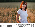 Woman stands in a golden field of wheat during sunset, showcasing natural beauty and serenity in a rural setting 130227714