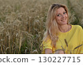 Woman sitting in a golden wheat field during sunset, capturing a serene moment of connection with nature under warm light 130227715