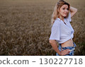 Woman sitting in a golden wheat field during sunset, capturing a serene moment of connection with nature under warm light 130227718