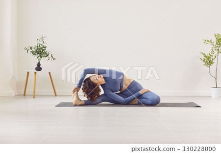 Young yogi woman wearing sportswear practising yoga on mat, student doing Revolved Head to Knee 130228000