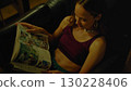 Young woman relaxing on couch reading magazine at night 130228406