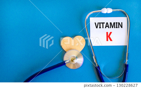 Vitamin K phylloquinone symbol. Concept words Vitamin K on beautiful white card. Wooden heart and stethoscope. Beautiful blue background. Medical healthy lifestyle Vitamin K phylloquinone concept. 130228627