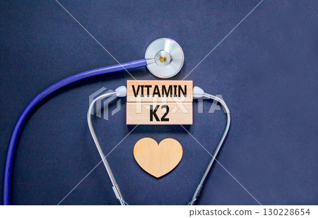Vitamin K2 phylloquinone symbol. Concept words Vitamin K2 on beautiful wooden blocks. Wooden heart stethoscope. Beautiful black background. Medical healthy lifestyle Vitamin K2 phylloquinone concept. 130228654