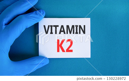 Vitamin K2 phylloquinone symbol. Concept words Vitamin K2 on beautiful card. Doctor's hand in blue medical glove. Beautiful blue background. Medical healthy lifestyle Vitamin K2 phylloquinone concept. Vitamin K2 phylloquinone symbol. Concept words Vitamin K2 on beautiful card. Doctor's hand in blue medical glove. Beautiful blue background. Medical healthy lifestyle Vitamin K2 phylloquinone concept. 130228972