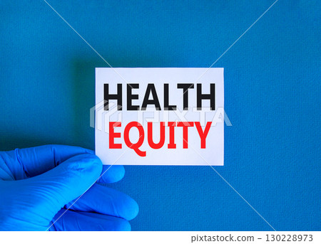 Health equity symbol. Concept words Health equity on beautiful white card. Doctor's hand in blue medical glove. Beautiful blue background. Medical healthy lifestyle health equity concept. Health equity symbol. Concept words Health equity on beautiful white card. Doctor's hand in blue medical glove. Beautiful blue background. Medical healthy lifestyle health equity concept. 130228973