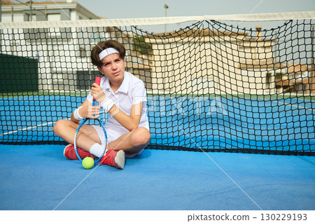 Young Tennis Player Resting by Net on Outdoor Court 130229193