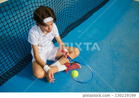 Young Tennis Player Resting on the Court Near the Net in Contemplation 130229199
