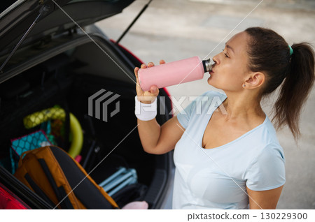 Woman Rehydrating Near Her Car After a Workout Session 130229300