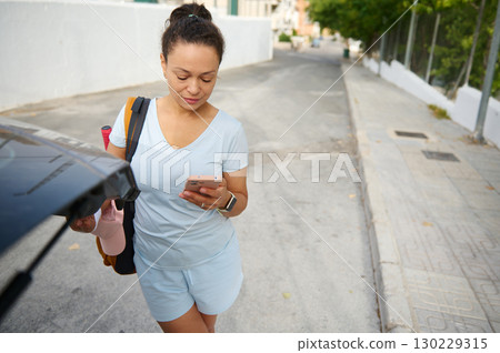 Woman Walking Outdoors While Checking Her Phone and Carrying a Bag Woman Walking Outdoors While Checking Her Phone and Carrying a Bag 130229315