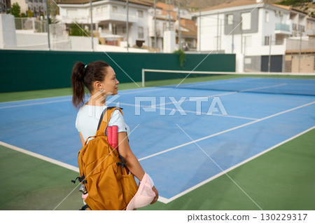 Young Girl With Backpack Standing By Tennis Court in Urban Area 130229317