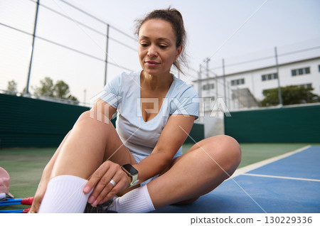 Woman Preparing for Sports on Outdoor Court with Focused Expression Woman Preparing for Sports on Outdoor Court with Focused Expression 130229336