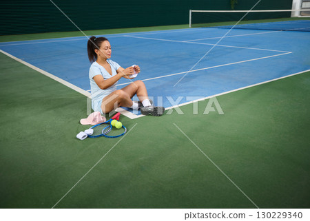 Young Woman Resting During Tennis Training on Outdoor Court 130229340