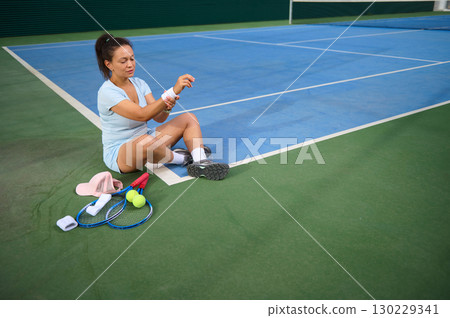 Female Tennis Player Resting on Court After Practice Session 130229341