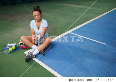 Woman Sitting on Tennis Court Resting After Practice Session Woman Sitting on Tennis Court Resting After Practice Session 130229342