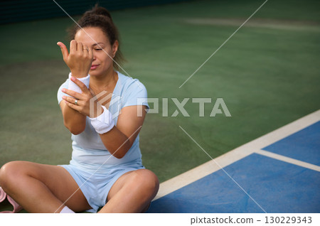 Woman Adjusting Wristbands on a Tennis Court in Sportswear Woman Adjusting Wristbands on a Tennis Court in Sportswear 130229343