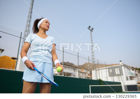 Female Tennis Player Standing Outdoors Holding Equipment and Looking Confident Female Tennis Player Standing Outdoors Holding Equipment and Looking Confident 130229365