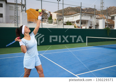 Female Tennis Player Preparing to Serve on Outdoor Court 130229371