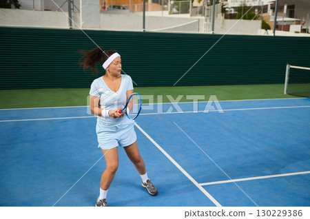 Female Tennis Player Swinging Racket on Outdoor Court During Match 130229386