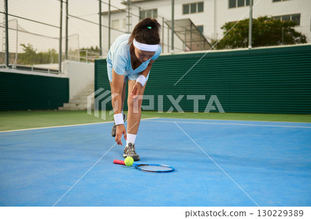 Young Woman Playing Tennis Retrieving Ball on Outdoor Court Young Woman Playing Tennis Retrieving Ball on Outdoor Court 130229389