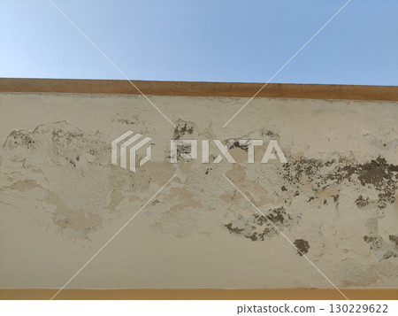 Close up of exterior wall with peeling paint and visible damage under blue sky Close up of exterior wall with peeling paint and visible damage under blue sky 130229622