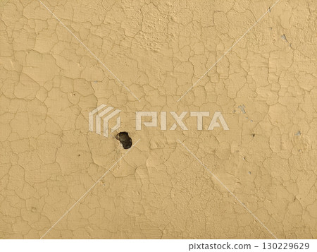 Close up of cracked beige paint with a small hole in the center surface 130229629
