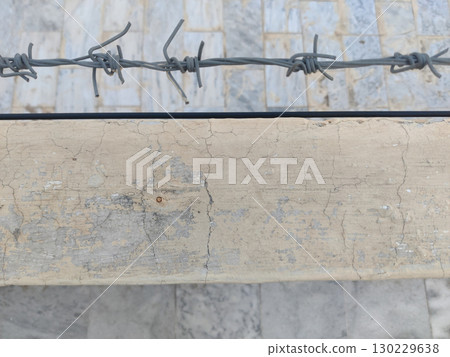 Close up of barbed wire over a concrete wall with cracked and aged paint 130229638