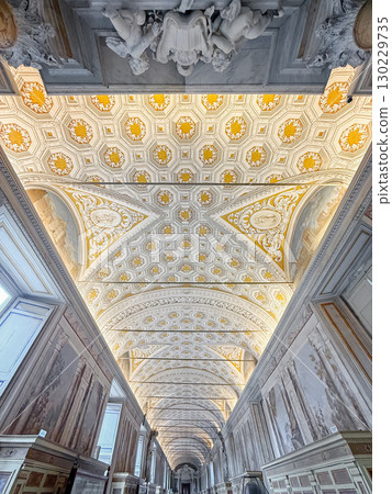 A stunning view down the long, vaulted ceiling of a gallery inside Vatican Museums. Masterpiece of geometric patterns, featuring intricate hexagonal designs in gold and white 130229735