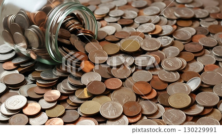Coins pouring from an overturned jar on a flat surface highlighting personal finance and saving strategies 130229991