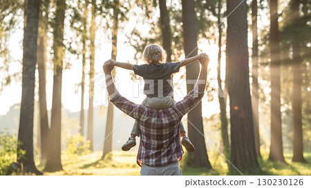 A father carries his son on his shoulders in a sunlit forest scenery view 130230126